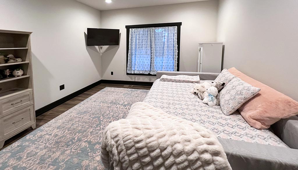 Photo of a light gray bedroom with a large area rug, a bed, and a mounted television