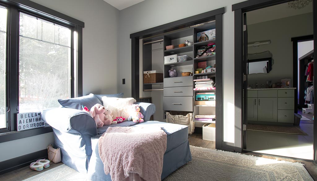 Photo of a room with light gray walls, a large sunny window, a comfortable chair, and a closet for storage