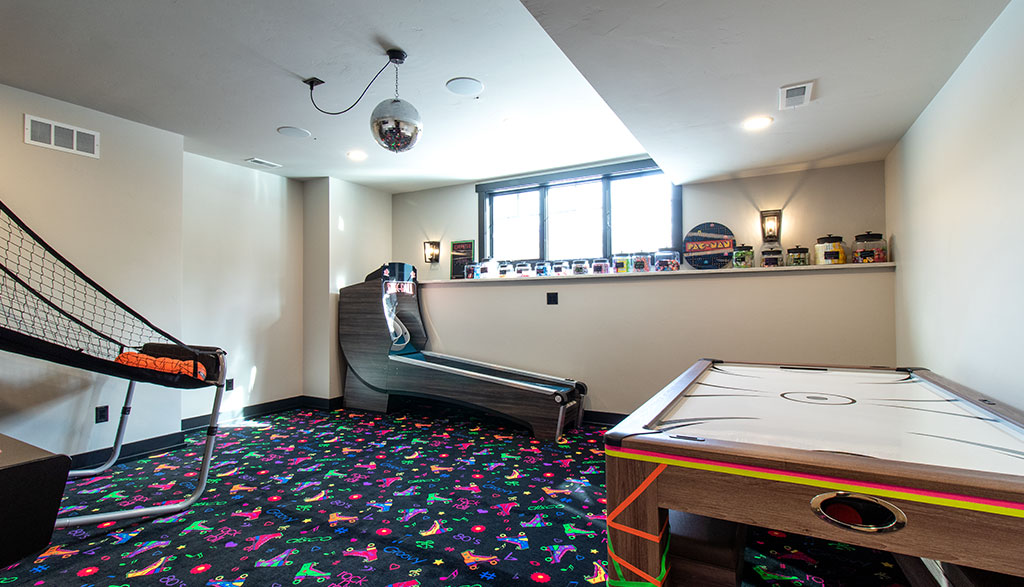 Arcade space with black and neon patterned floor, with air hockey table, skee ball, and basketball game